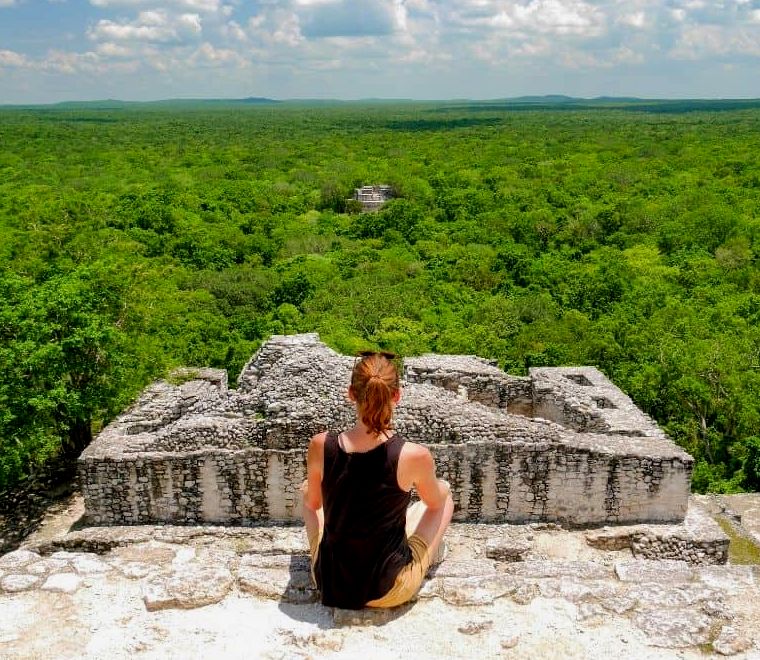 mulher com uma blusa preta sentada no topo da pirâmide maia nas selvas do México, ruínas de Calakmul, um dos lugares mais exclusivos para se visitar no México