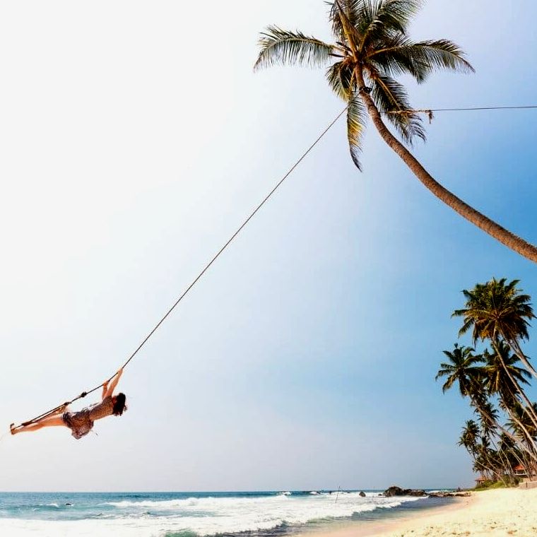 Mulher feliz em um balanço de árvore na praia |  Ansiedade de viajar sozinho
