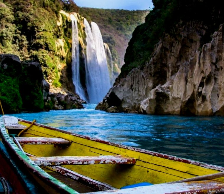 velho barco amarelo de madeira em primeiro plano e cachoeira em segundo plano em Huasteca Potosina, um dos lugares mais exclusivos para visitar no México