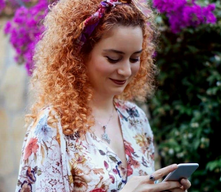 Mulher com cabelos ruivos olhando para o celular |  Ansiedade de viajar sozinho