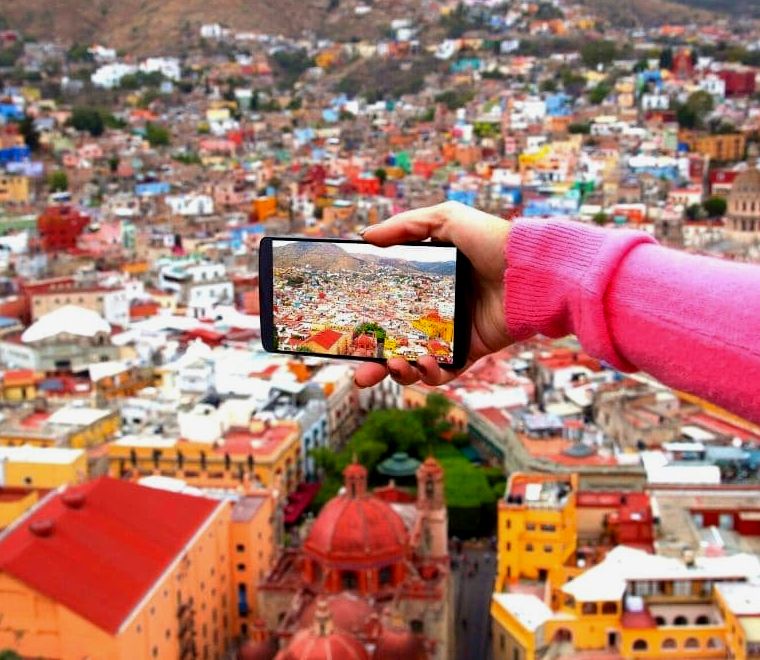 mãos segurando um iphone e tirando uma foto de uma cidade colorida