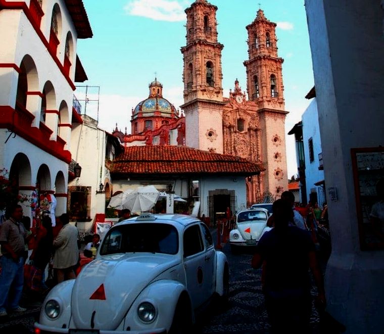 dois velhos carros VW Bug brancos percorrem as pequenas ruas de paralelepípedos da cidade colonial de Taxco, um dos lugares mais exclusivos para se visitar no México