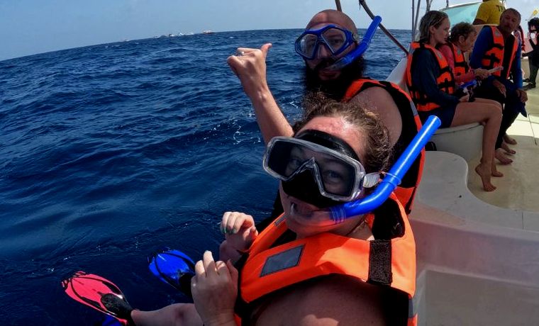 duas pessoas em um barco com coletes salva-vidas, máscaras e snorkels prestes a pular no oceano