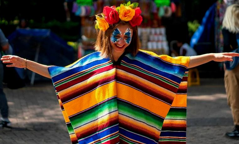 mulher com o rosto pintado usando um poncho de cores vivas durante a celebração do Dia dos Mortos no Parque Aquático Xcaret na Riviera Maya, México