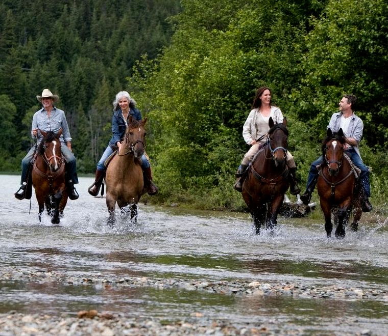 duas mulheres e dois homens andando a cavalo por um rio