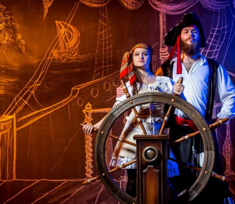 homem e mulher vestindo fantasias de pirata segurando as rodas do navio pirata