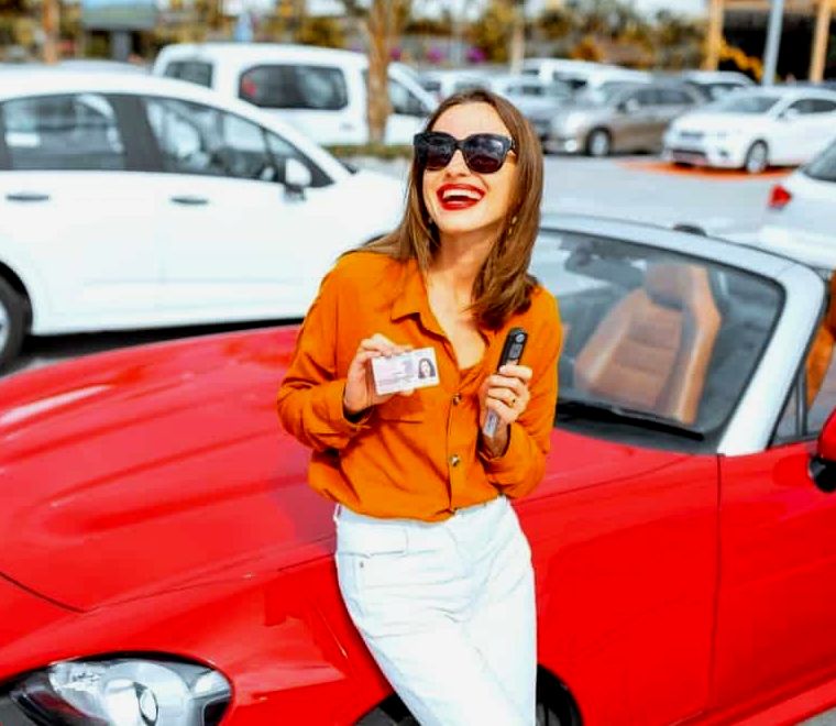 mulher apoiada em um carro esporte conversível vermelho e segurando sua licença e a chave |  alugar um carro no México